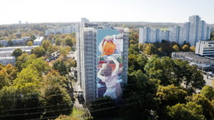 großes Wandbild an einem Hochhaus. Zu sehen ist ein Kind, eine S-Bahn und eine Hand, die eine orangene Gießkanne hält