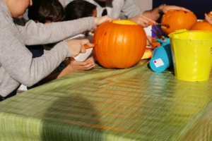 2 Erwachsene und 2 Kinder sitzen an einem Tisch mit grüner Tischdecke und schnitzen einen orangefarbenen Kürbis